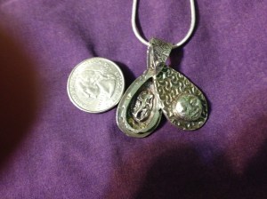 LIZARD HATCHES THE MOON. This hollow-form pendant bears a moon on its face and, inside, a lizard sits on a nest of cubic zirconia eggs. 